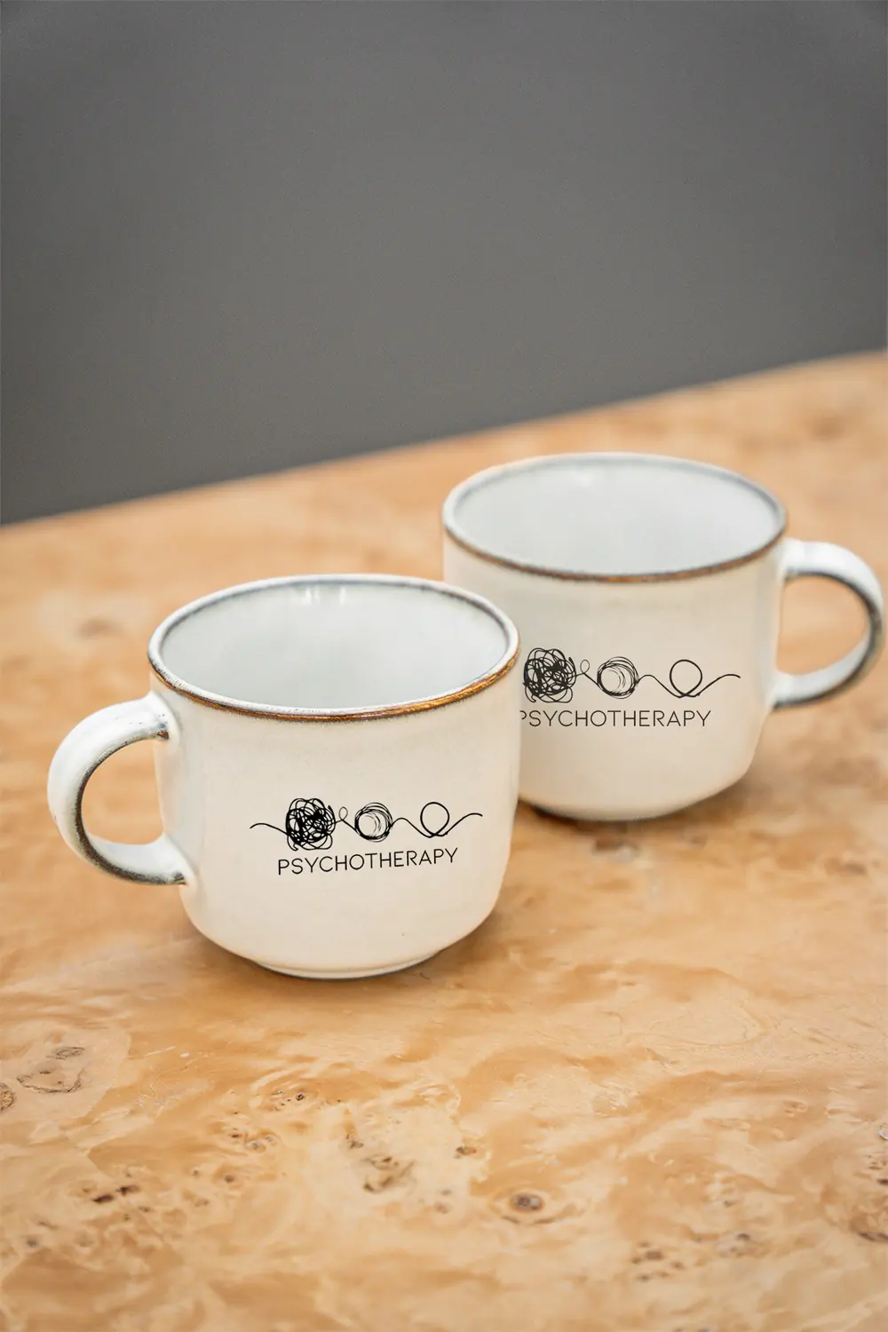 Two Jhanelle Peters Psychotherapy mugs on a wooden table