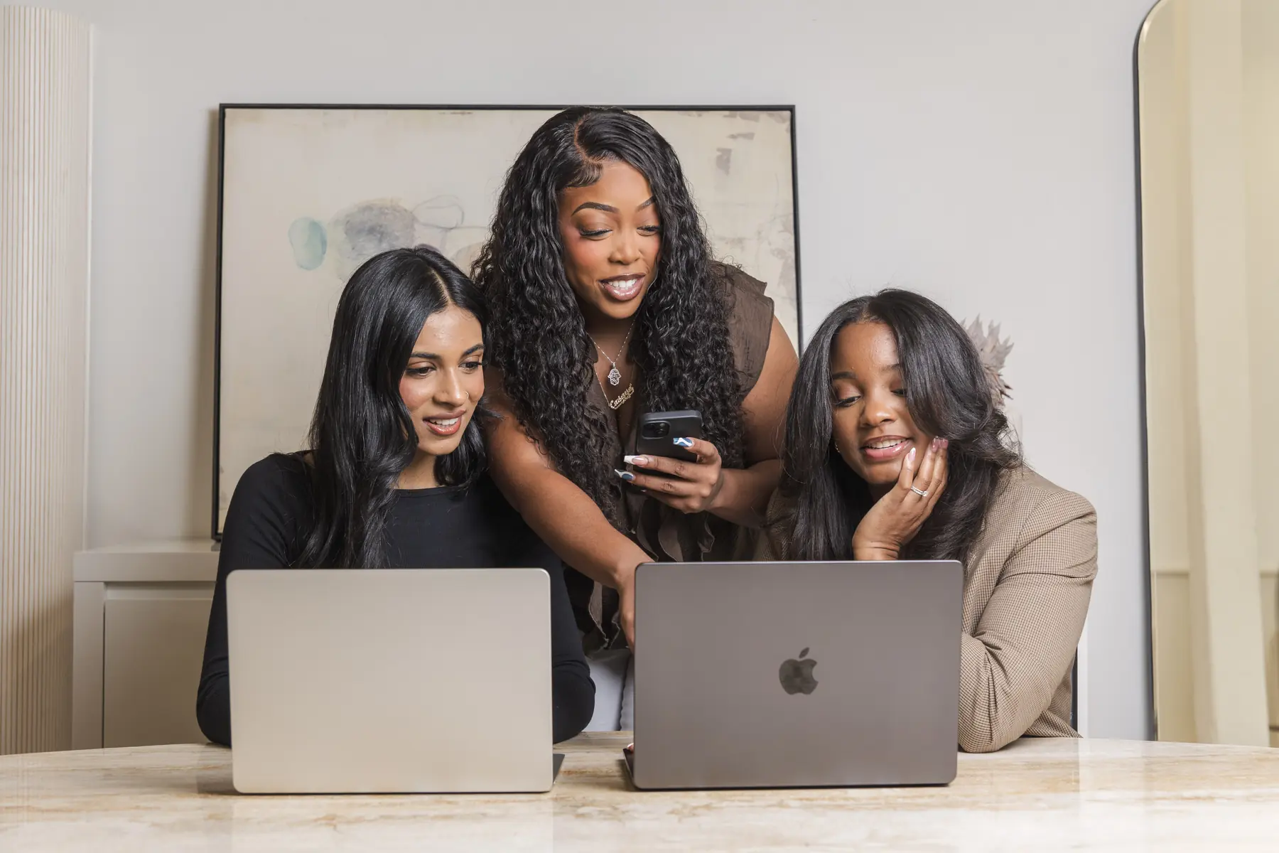 Three team members looking at a phone together at their laptops